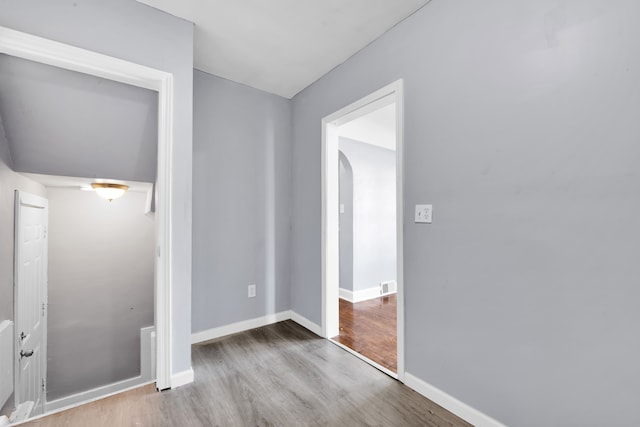 unfurnished bedroom featuring arched walkways, wood finished floors, visible vents, baseboards, and a closet