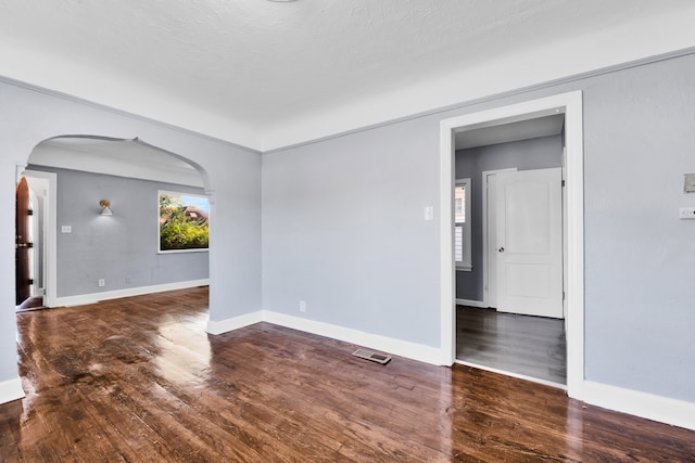 spare room featuring arched walkways, wood finished floors, visible vents, and baseboards