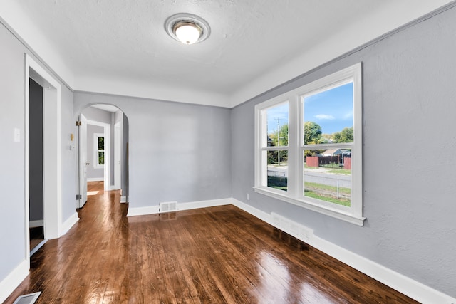 empty room with arched walkways, dark wood-style floors, visible vents, and baseboards