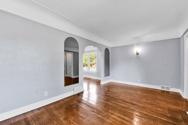 unfurnished room featuring arched walkways, visible vents, baseboards, and wood finished floors