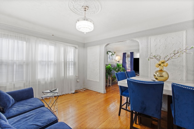 dining area featuring arched walkways, a chandelier, light wood finished floors, and a textured wall