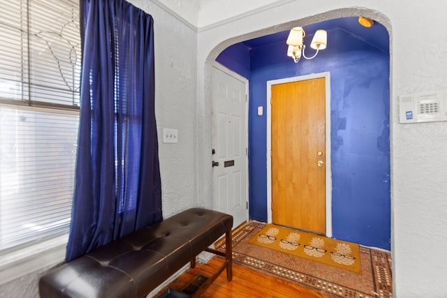 foyer featuring arched walkways, a notable chandelier, wood finished floors, and a textured wall
