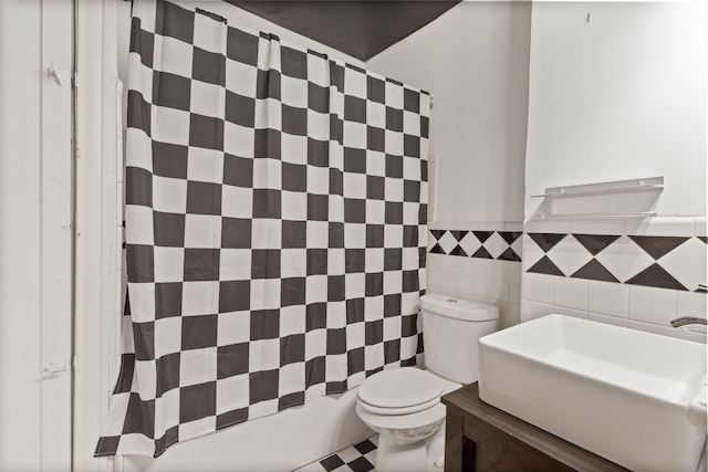 bathroom with curtained shower, toilet, wainscoting, tile walls, and a sink