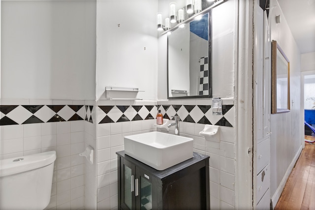 half bath with tile walls, toilet, wainscoting, wood finished floors, and vanity