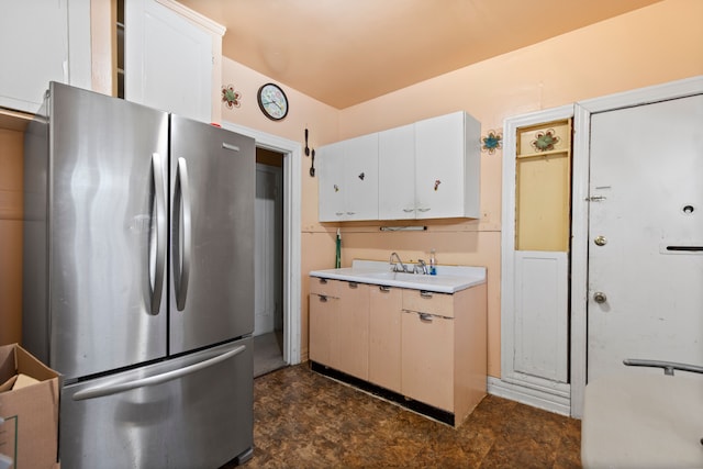 kitchen featuring stone finish floor, light countertops, freestanding refrigerator, white cabinets, and a sink