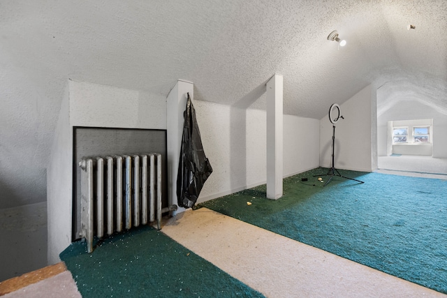 additional living space with a textured ceiling, carpet floors, radiator, and vaulted ceiling