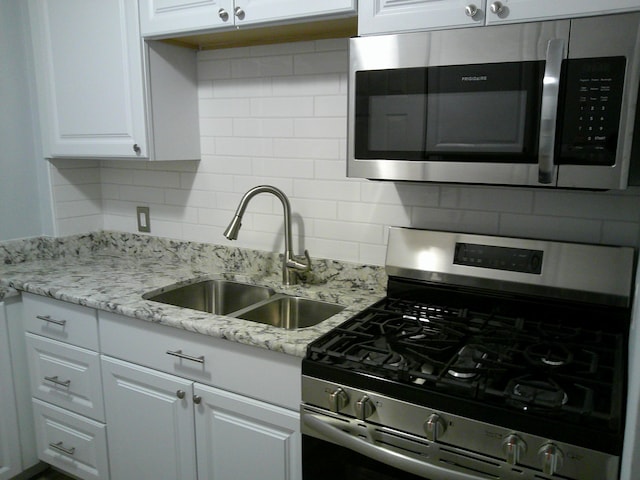 kitchen featuring stainless steel appliances, a sink, white cabinets, decorative backsplash, and light stone countertops