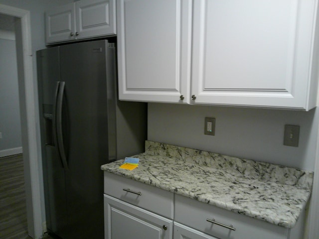 kitchen featuring dark wood-style floors, black fridge, white cabinetry, and baseboards