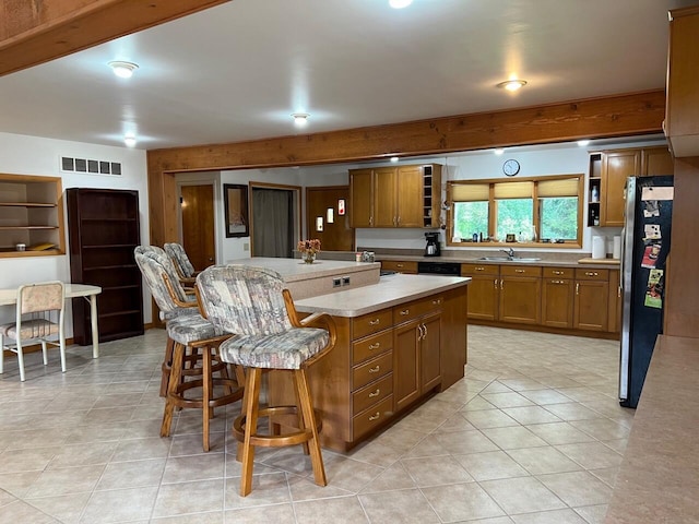 kitchen featuring brown cabinetry, a kitchen island, freestanding refrigerator, open shelves, and a sink