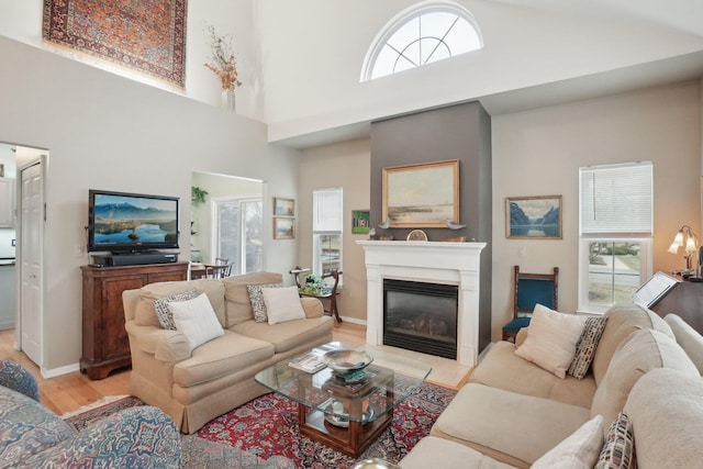 living room featuring a glass covered fireplace, wood finished floors, a towering ceiling, and baseboards