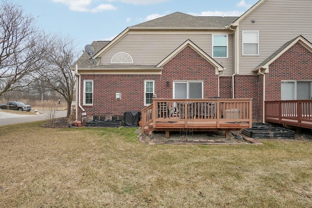 back of house featuring a shingled roof, brick siding, a lawn, and a deck