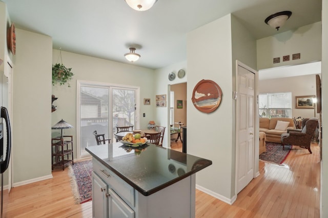 kitchen featuring a center island, light wood finished floors, dark countertops, freestanding refrigerator, and baseboards