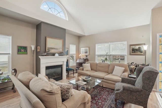 living room with high vaulted ceiling, light wood-type flooring, and a glass covered fireplace