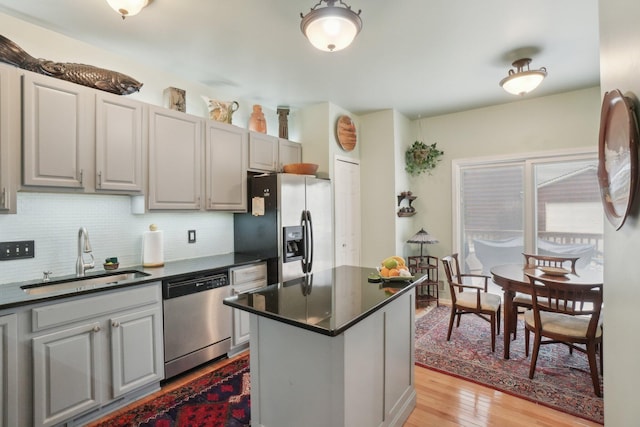 kitchen with light wood finished floors, tasteful backsplash, dark countertops, stainless steel appliances, and a sink