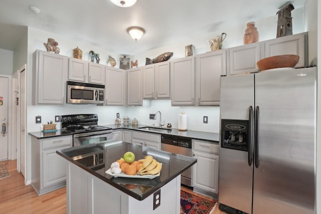 kitchen with stainless steel appliances, dark countertops, tasteful backsplash, light wood-style floors, and a sink