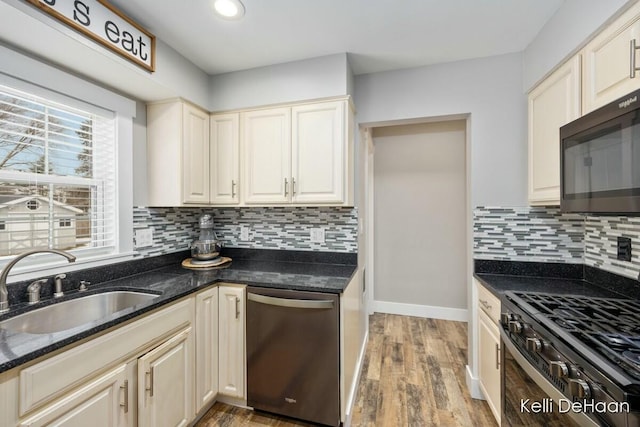 kitchen with tasteful backsplash, appliances with stainless steel finishes, a sink, dark stone countertops, and light wood-type flooring