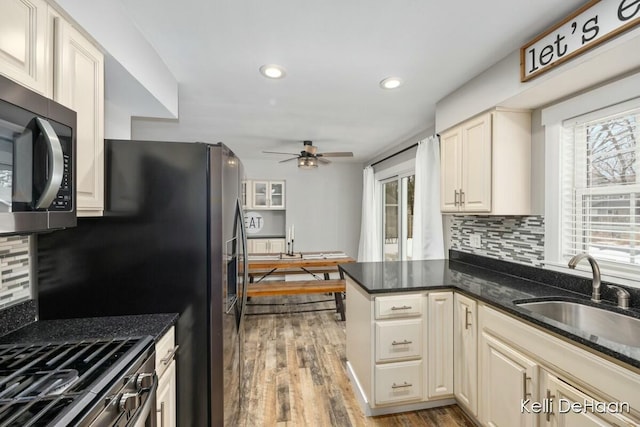 kitchen with stainless steel microwave, a peninsula, a sink, light wood-style floors, and backsplash