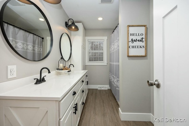 full bathroom featuring double vanity, baseboards, visible vents, wood finished floors, and a sink