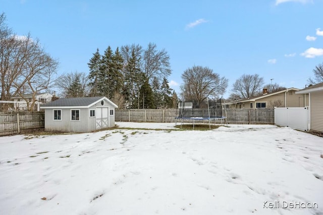 yard layered in snow with an outbuilding, a storage shed, a trampoline, and a fenced backyard