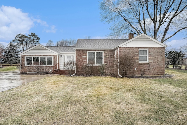 view of front facade with a shingled roof, a front yard, brick siding, and a chimney