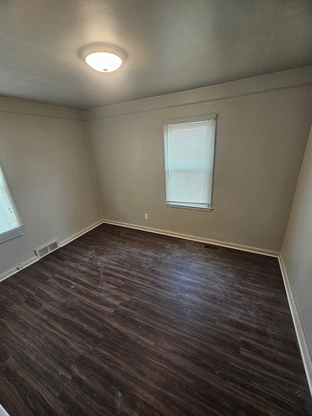 unfurnished room with a wealth of natural light, visible vents, dark wood finished floors, and baseboards