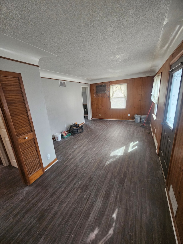 unfurnished living room featuring dark wood-style flooring, visible vents, wood walls, a textured ceiling, and baseboards