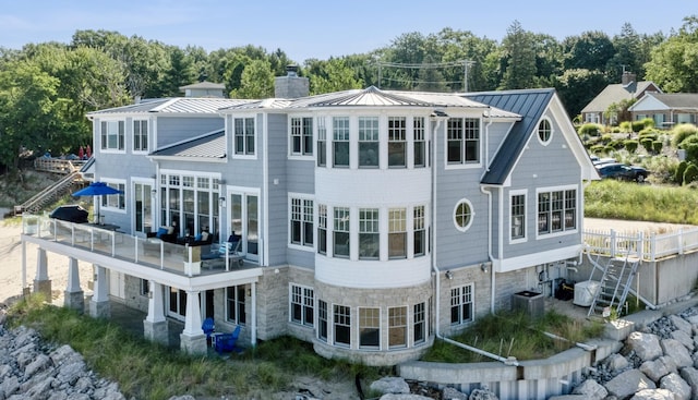 back of property featuring metal roof, a standing seam roof, a chimney, and stone siding