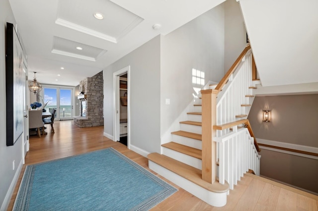 stairs with baseboards, a raised ceiling, wood finished floors, an inviting chandelier, and recessed lighting