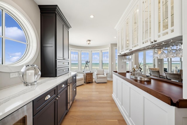 kitchen with recessed lighting, white cabinets, dark stone counters, light wood finished floors, and glass insert cabinets
