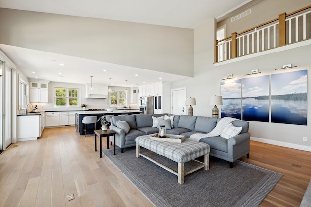 living room with recessed lighting, visible vents, a towering ceiling, light wood-style floors, and baseboards