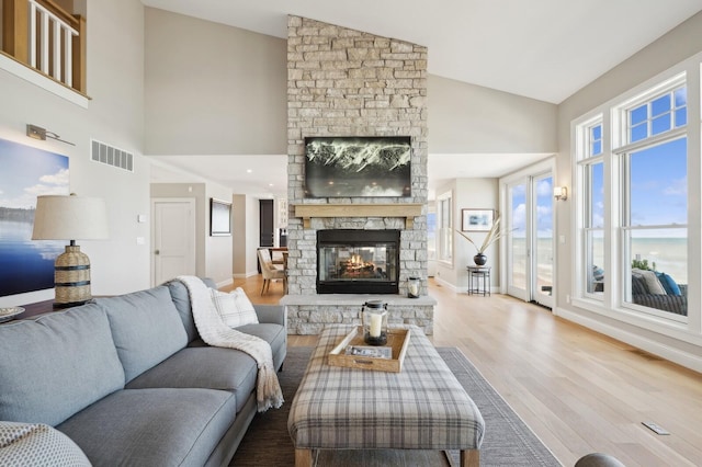 living area featuring visible vents, a stone fireplace, wood finished floors, high vaulted ceiling, and baseboards