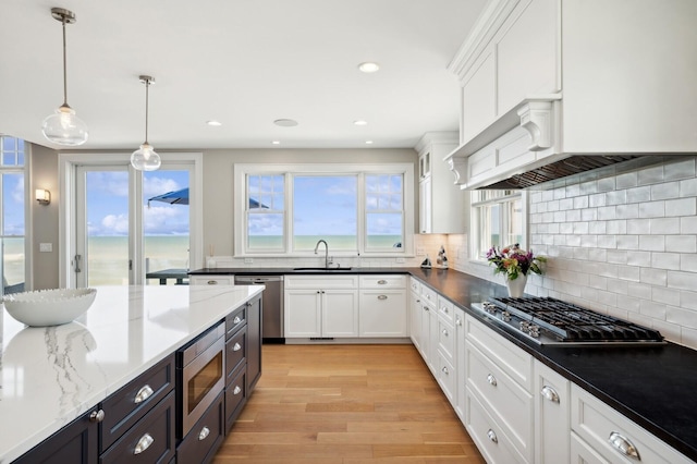 kitchen featuring decorative backsplash, appliances with stainless steel finishes, white cabinets, a sink, and light wood-type flooring