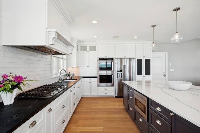 kitchen featuring white cabinets, light wood-style flooring, stainless steel appliances, pendant lighting, and a sink