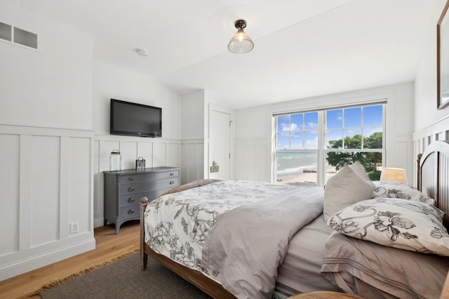 bedroom with wainscoting, visible vents, and light wood finished floors