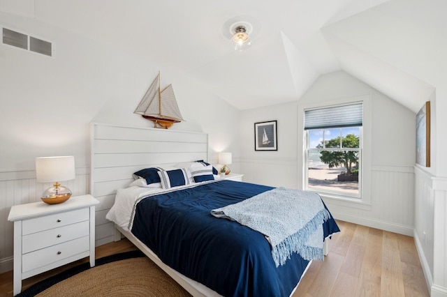 bedroom featuring vaulted ceiling, wainscoting, light wood-type flooring, and visible vents