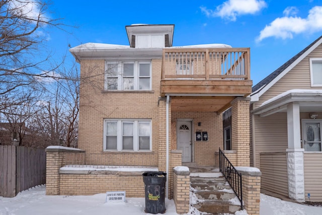 view of front of home with brick siding, fence, and a balcony