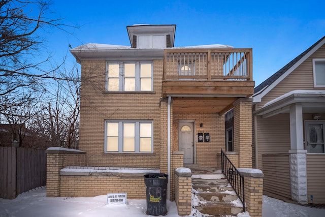 view of front facade featuring covered porch, brick siding, fence, and a balcony