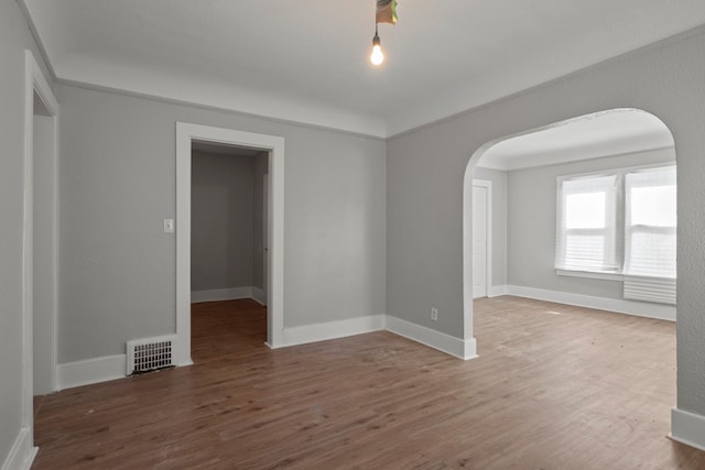 unfurnished room featuring arched walkways, visible vents, baseboards, and wood finished floors