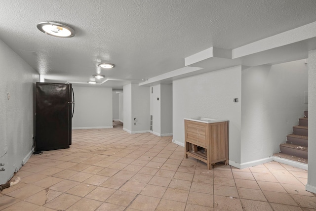 finished basement featuring a textured ceiling, light tile patterned floors, baseboards, stairway, and freestanding refrigerator