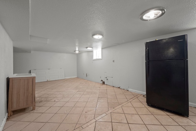 basement with light tile patterned floors, a textured ceiling, and freestanding refrigerator