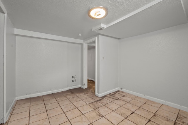 spare room featuring a textured ceiling, light tile patterned flooring, and baseboards