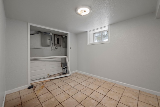 below grade area featuring a textured ceiling, a textured wall, light tile patterned floors, and baseboards