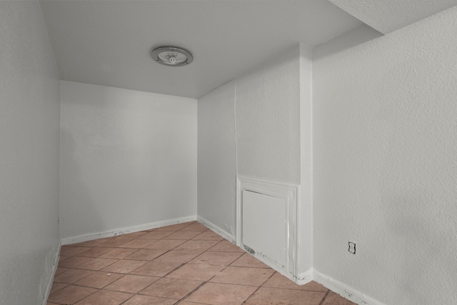 spare room with light tile patterned flooring, a textured wall, and baseboards