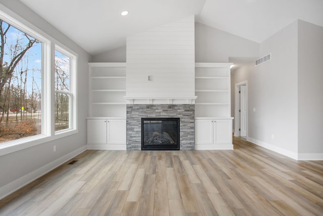 unfurnished living room with light wood-style floors, visible vents, vaulted ceiling, and a glass covered fireplace