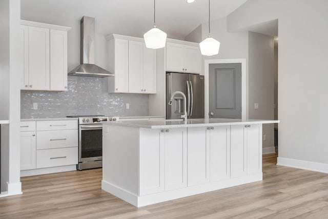 kitchen with a kitchen island with sink, white cabinetry, light countertops, appliances with stainless steel finishes, and wall chimney range hood