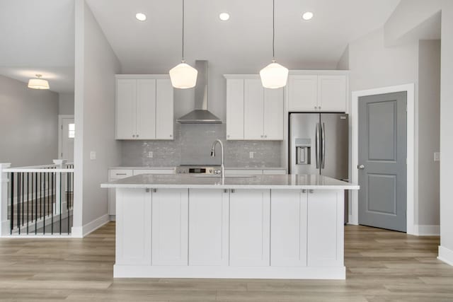 kitchen with light countertops, stainless steel fridge, an island with sink, and wall chimney exhaust hood