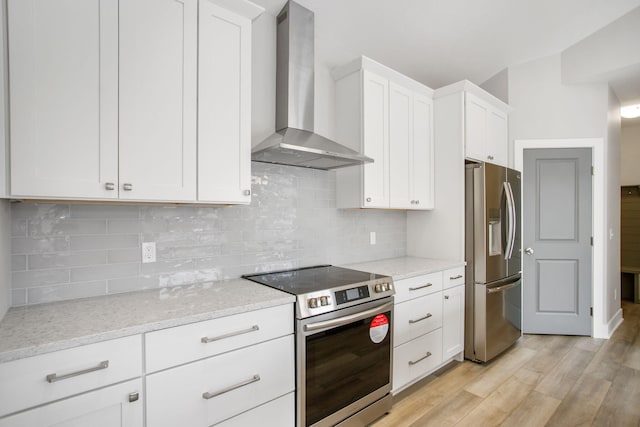 kitchen featuring light wood finished floors, white cabinets, wall chimney exhaust hood, appliances with stainless steel finishes, and light stone counters