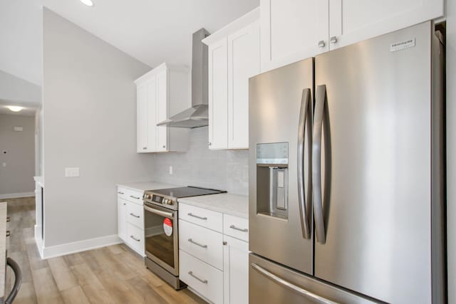 kitchen with stainless steel appliances, white cabinetry, wall chimney range hood, light wood-type flooring, and decorative backsplash