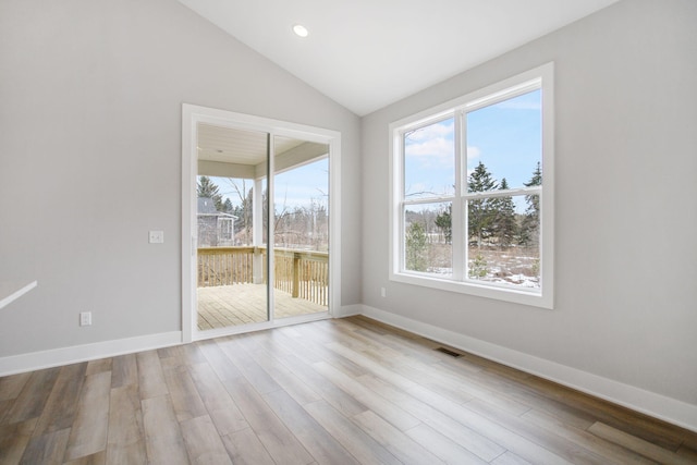 empty room featuring lofted ceiling, visible vents, baseboards, and wood finished floors