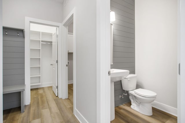 bathroom with baseboards, wood finished floors, toilet, and a walk in closet